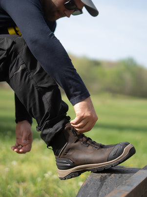 tradesman adjusting a boot safety workwear outdoors with grass and sky in the background