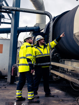 Two workers in high-visibility safety gear inspecting industrial equipment.